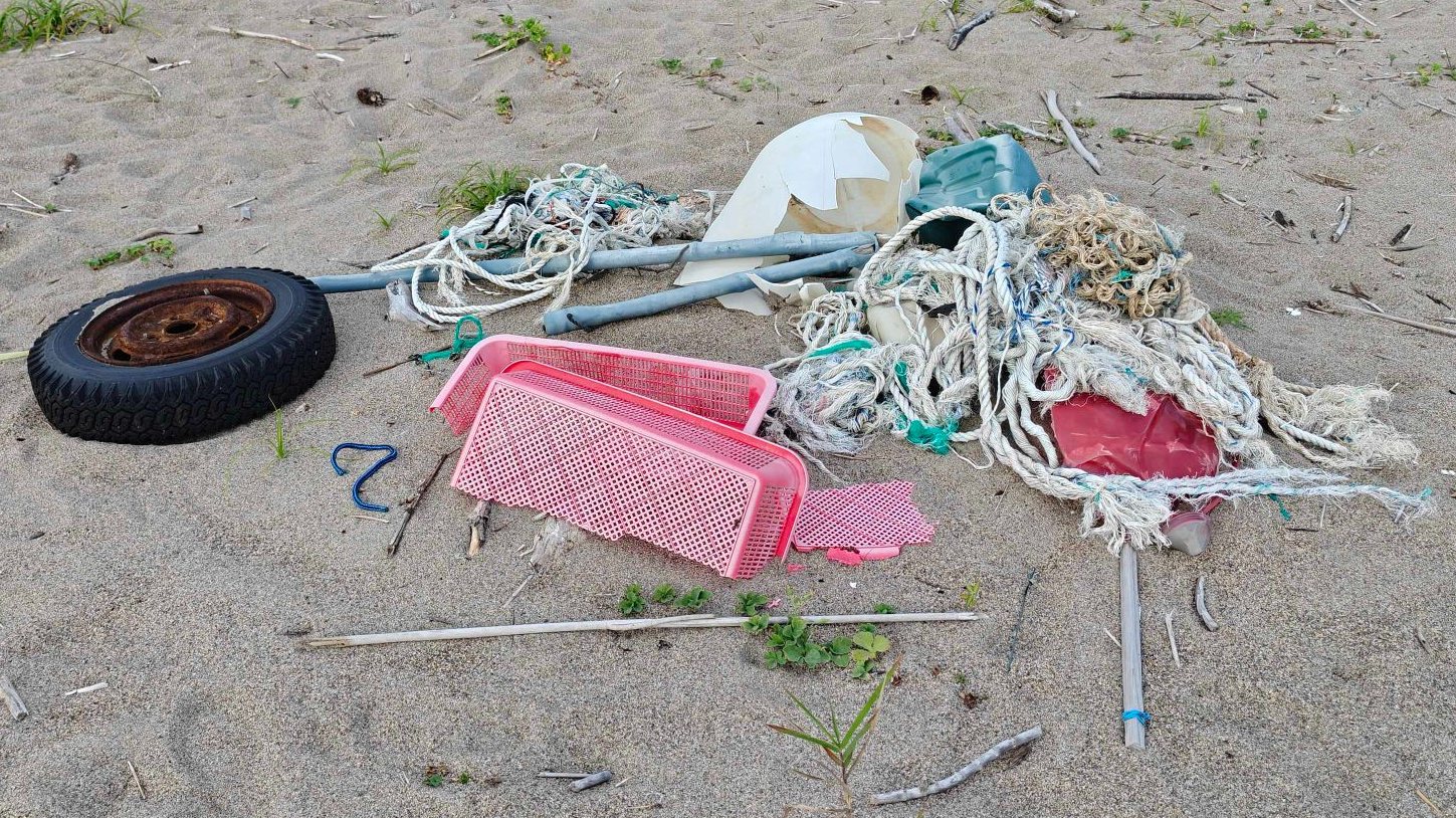 砂浜に漂着したロープ、漁網、かご、タイヤ